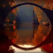 beautiful stone arch over calm body of water surrounded with autumn colors