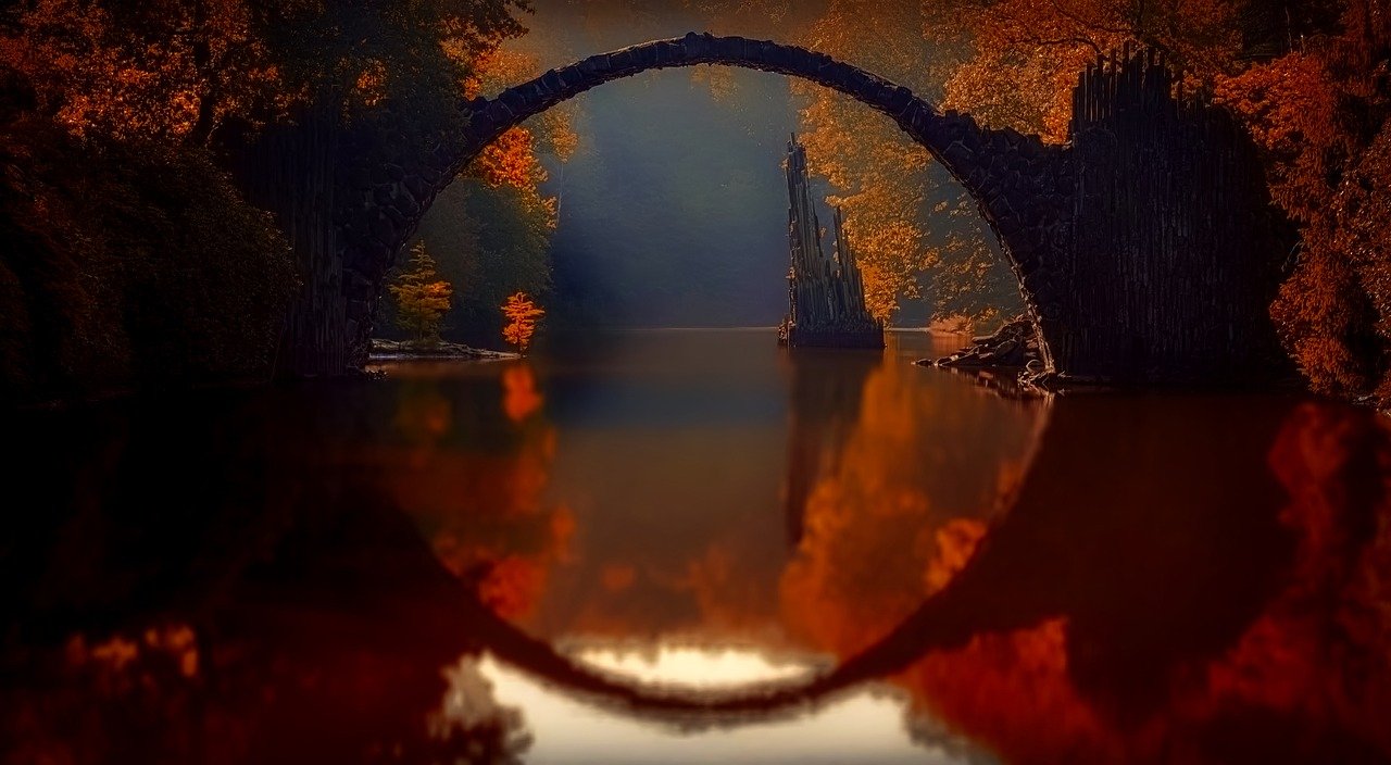 beautiful stone arch over calm body of water surrounded with autumn colors