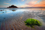 Tide going out on beach with seaweed in foreground and sky and island in distance.