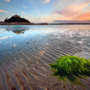 Tide going out on beach with seaweed in foreground and sky and island in distance.