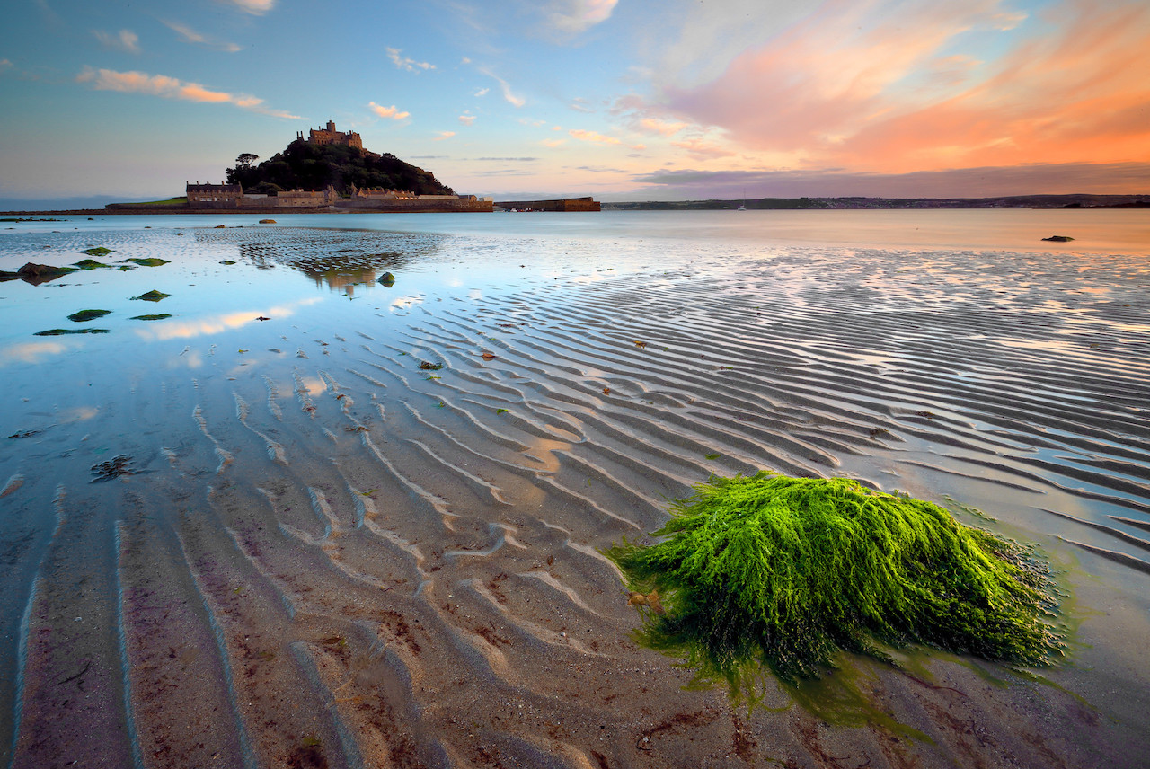 Tide going out on beach with seaweed in foreground and sky and island in distance.