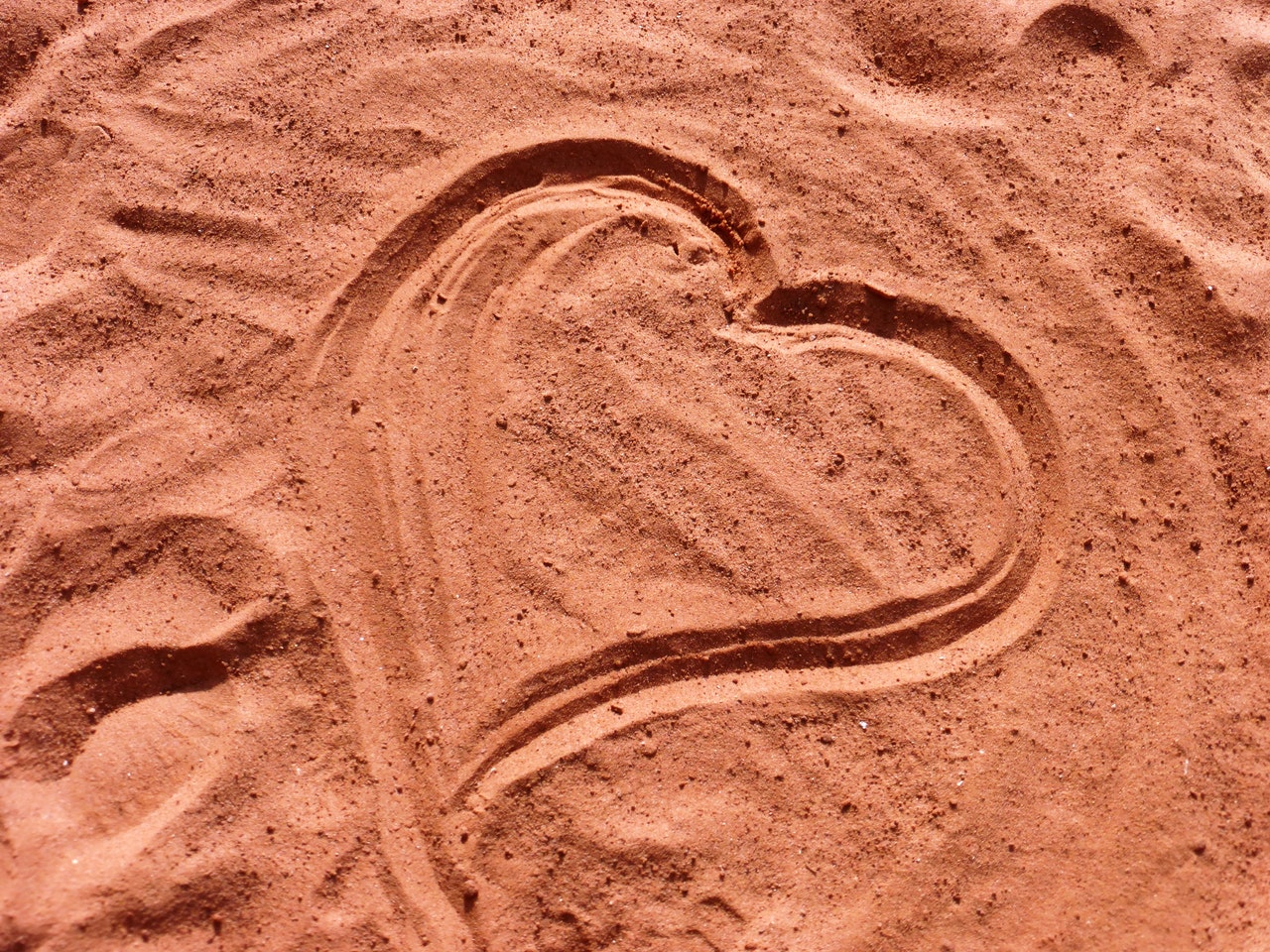 red-brown sand that a finger has drawn a heart in