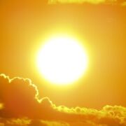 A very bright sun with a few clouds below it. The sky is golden.
