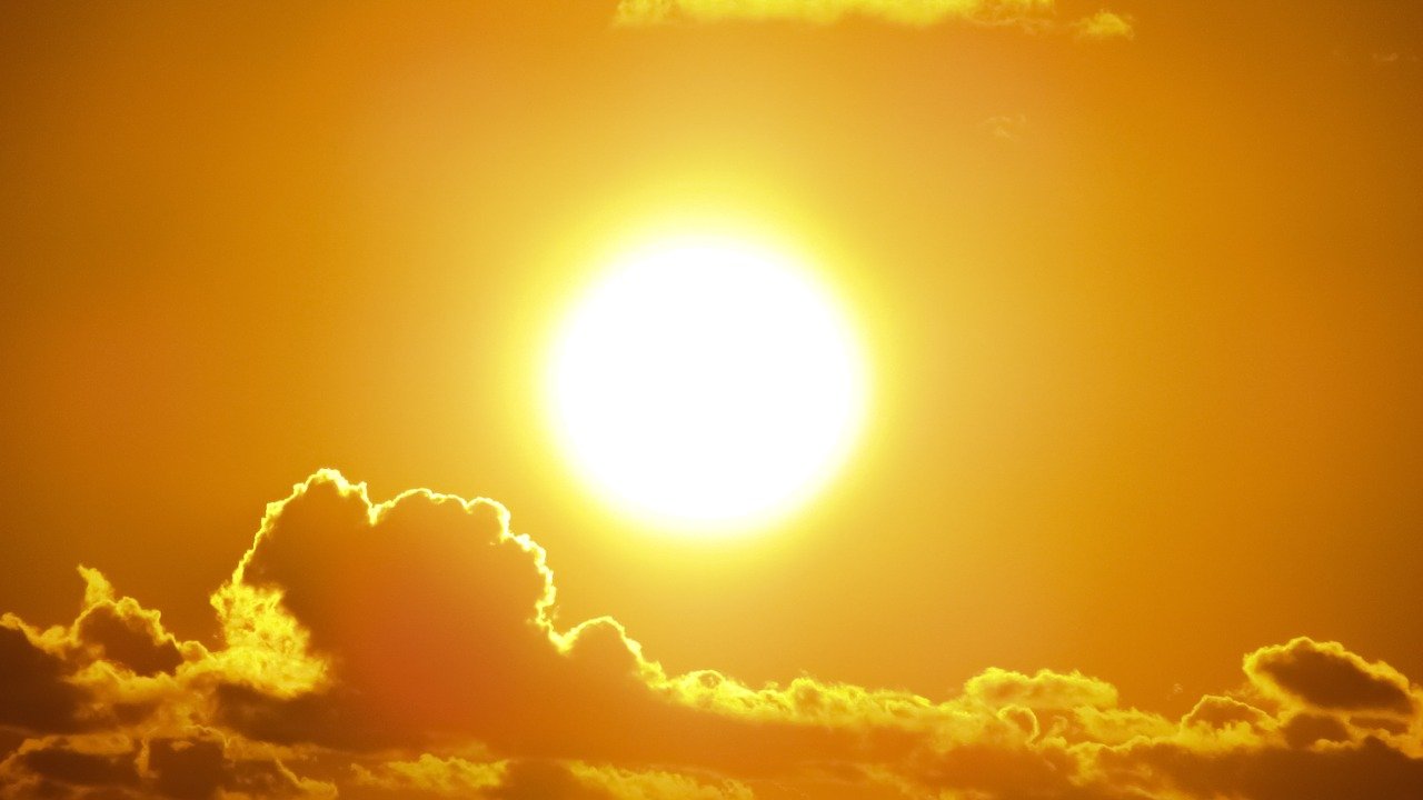 A very bright sun with a few clouds below it. The sky is golden.