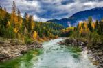 smooth flowing river with autumn trees, clouds in sky and mountains