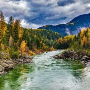 smooth flowing river with autumn trees, clouds in sky and mountains