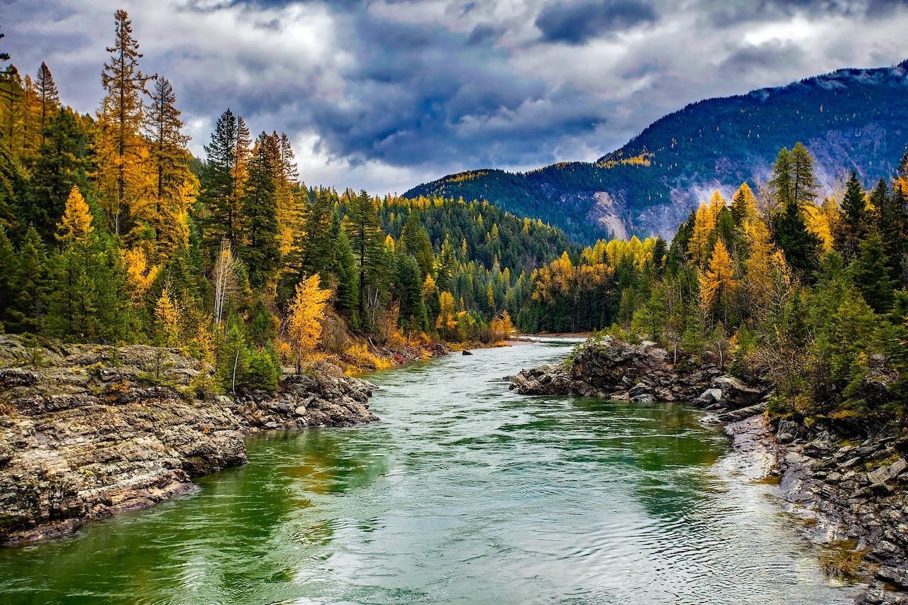 smooth flowing river with autumn trees, clouds in sky and mountains