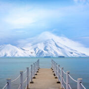 dock leading to blue water with beautiful snow-covered mountains in distance