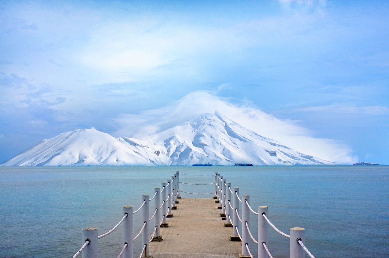dock leading to blue water with beautiful snow-covered mountains in distance
