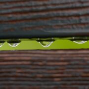 two small horizontal wood fence slabs with a small opening and four drops of water between them and bright green in the background seen through the opening