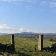 A green field and distant hills with two stone posts as an entryway