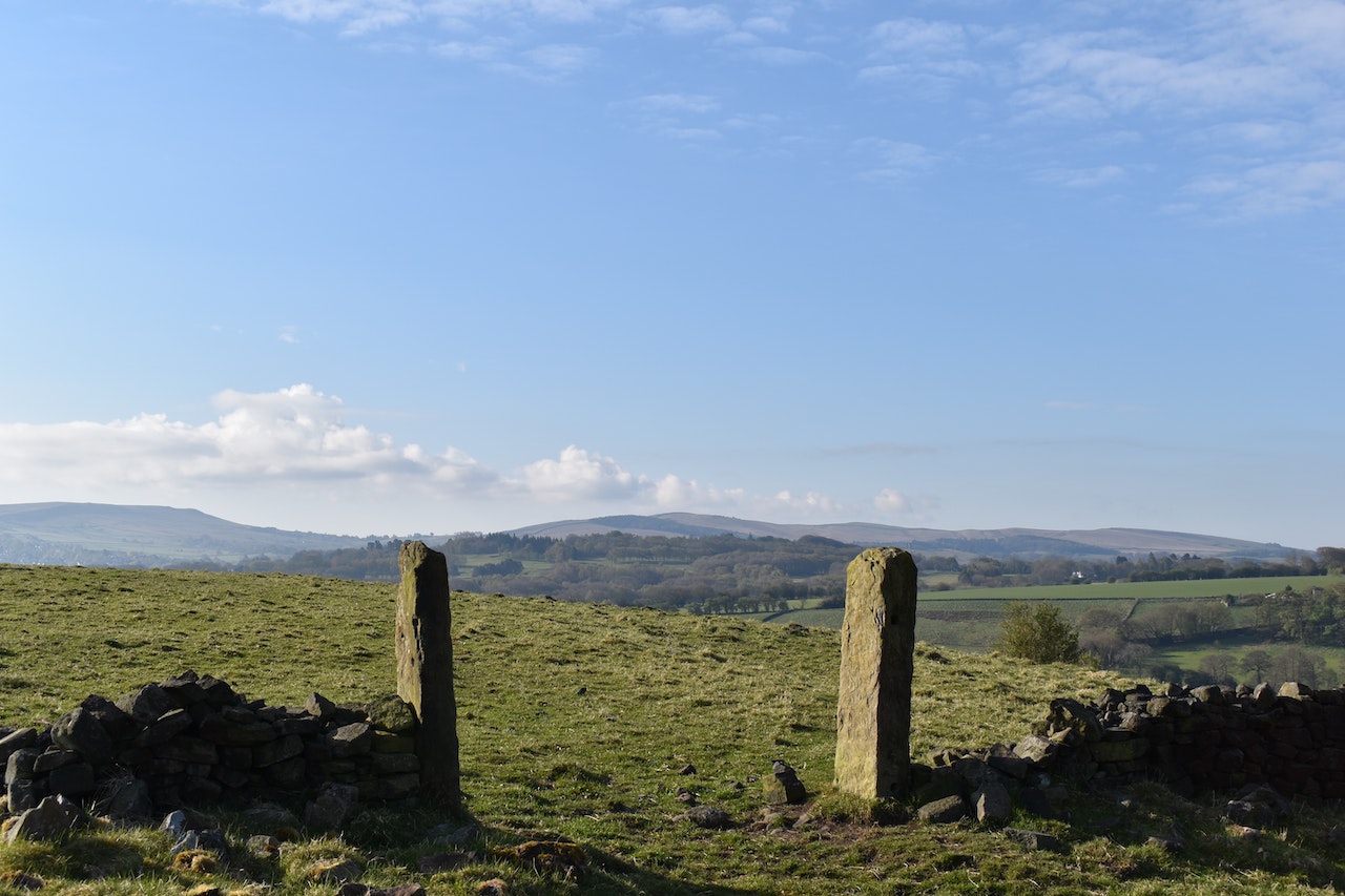 A green field and distant hills with two stone posts as an entryway