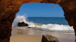 Looking out from a rock cave at ocean waves with birds flying high in the sky