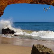 Looking out from a rock cave at ocean waves with birds flying high in the sky