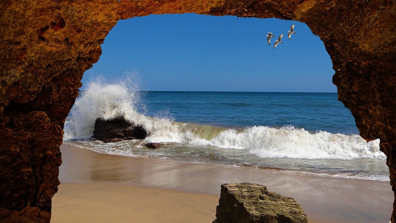 expandMarisa04pixabay Looking out from a rock cave at ocean waves with birds flying high in the sky