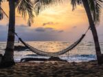 An empty hammock as the sun sets on a calm beach and ocean