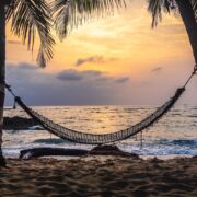 An empty hammock as the sun sets on a calm beach and ocean