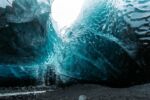 An ice cave with dramatic blue hues, leading to a white opening.