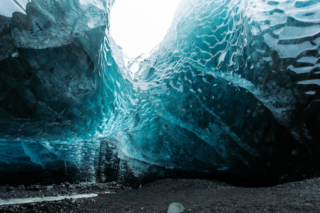 An ice cave with dramatic blue hues, leading to a white opening.