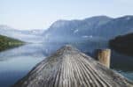 A smooth wooden dock reaching into a calm lake with mountains in background