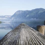 A smooth wooden dock reaching into a calm lake with mountains in background