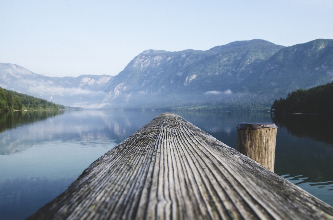 A smooth wooden dock reaching into a calm lake with mountains in background