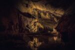 The interior of a dark cave with many features, lightly lit with gold light.