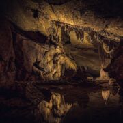 The interior of a dark cave with many features, lightly lit with gold light.
