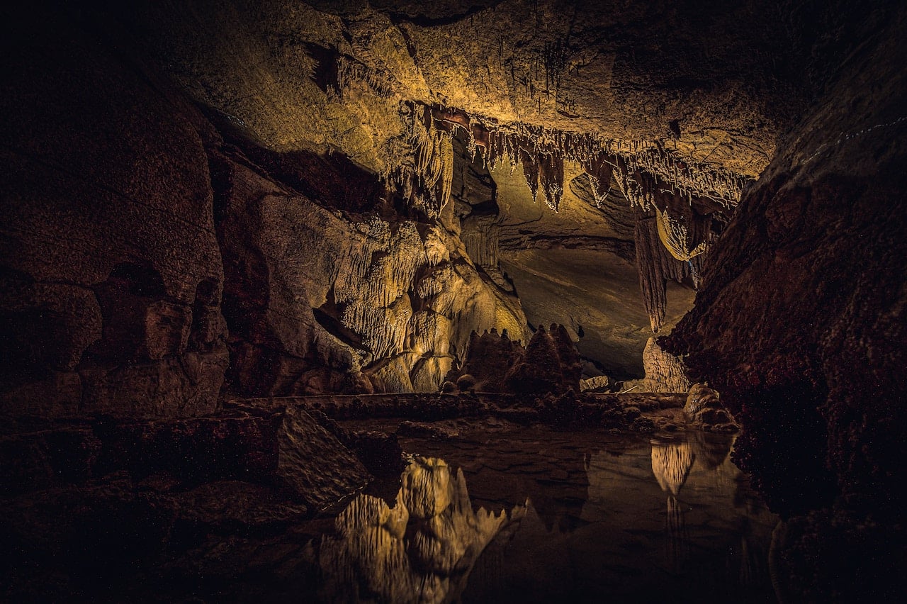 The interior of a dark cave with many features, lightly lit with gold light.