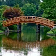 Curved wooden bridge over a calm river with green trees in background..