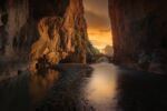 A smooth river surrounded by rock walls leading to an opening through a stone arch at sunset.