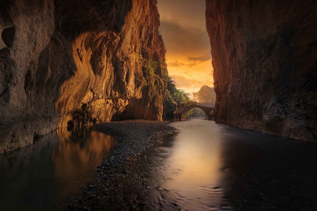 A smooth river surrounded by rock walls leading to an opening at sunset.
