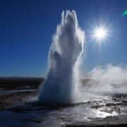 Geyser erupting against a bright blue sky and sun