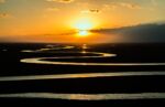 A winding river on flat land reflecting a golden sunset.