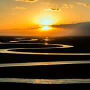 A winding river on flat land reflecting a golden sunset.
