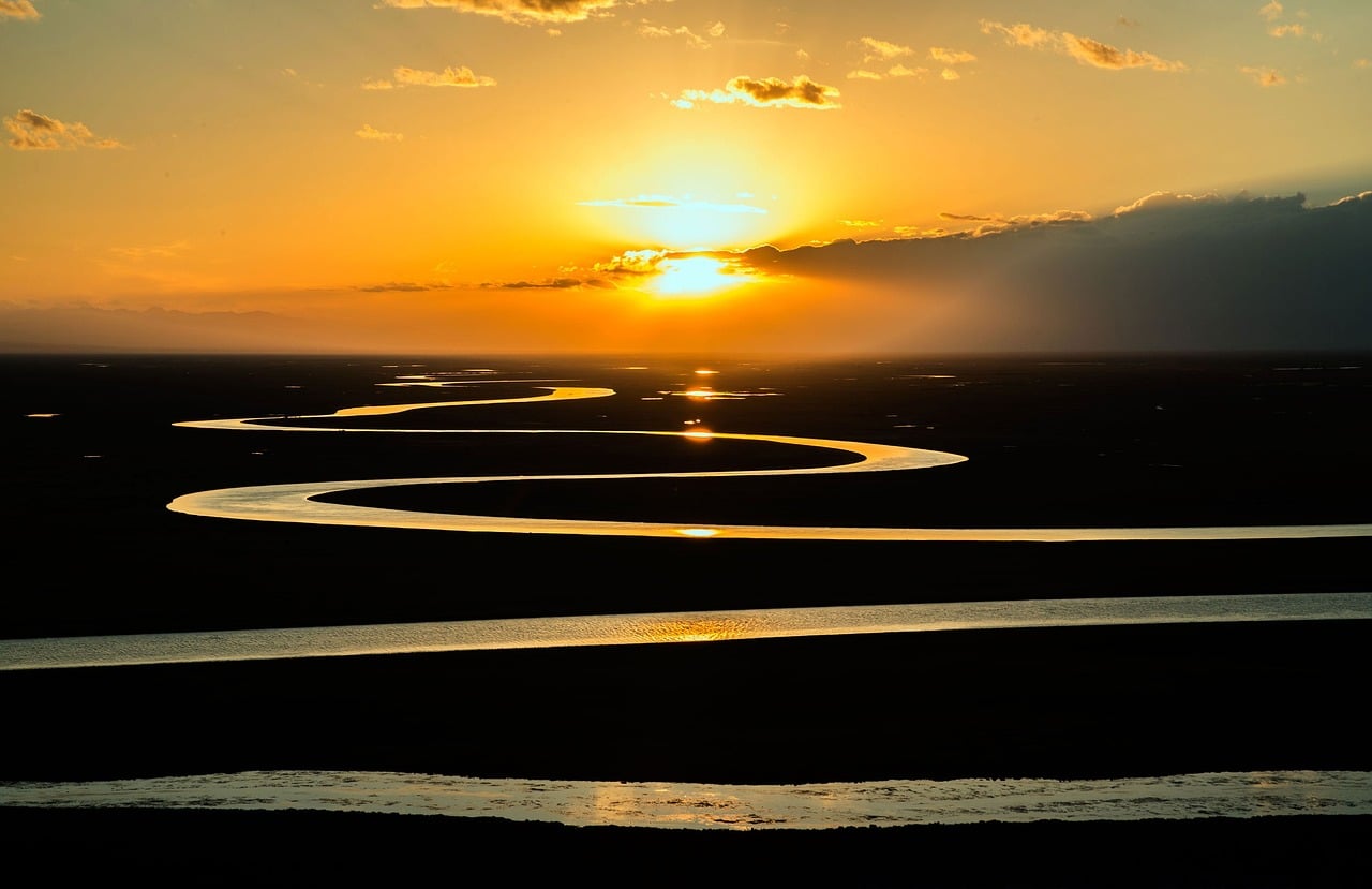 A winding river on flat land reflecting a golden sunset.