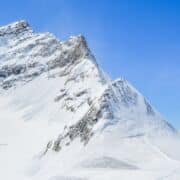 A rugged mountain peak, covered in snow, against a blue sky.