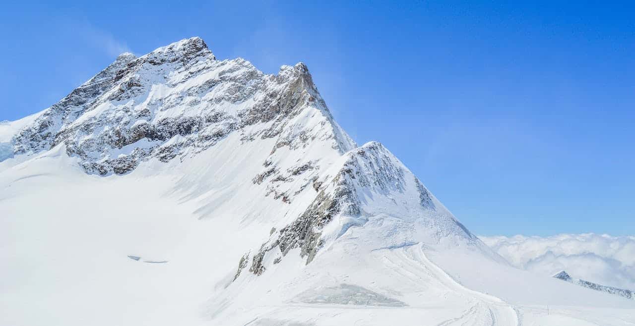 A rugged mountain peak, covered in snow, against a blue sky. 