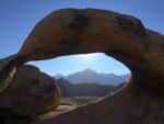 A rock arch beyond which we can see blue sky and mountains.