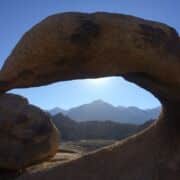 A rock arch beyond which we can see blue sky and mountains.