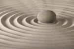 Pink/beige sand raked in perfect circles like a zen garden with a stone in center