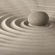 Pink/beige sand raked in perfect circles like a zen garden with a stone in center