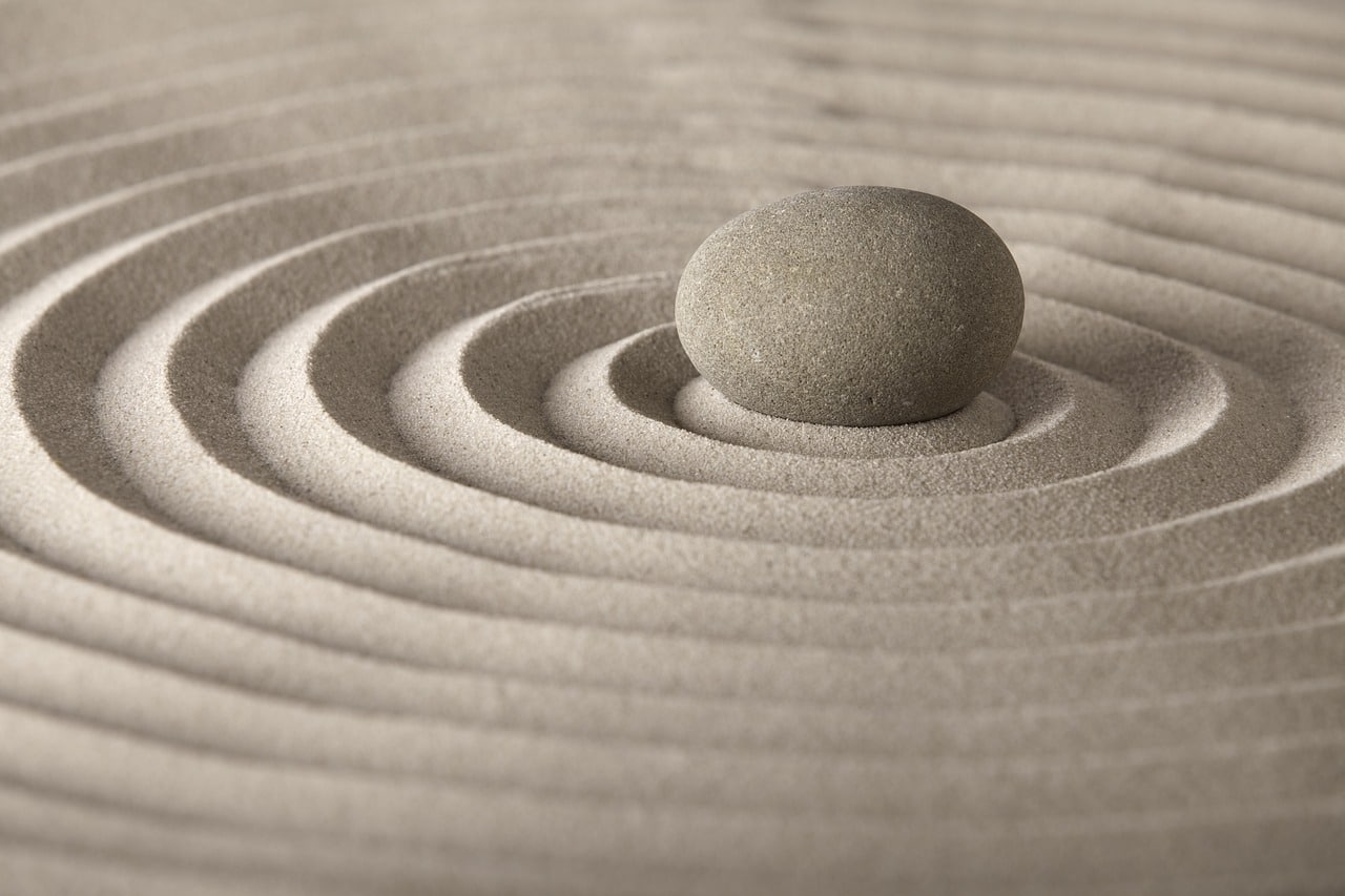 Pink/beige sand raked in perfect circles like a zen garden with a stone in center