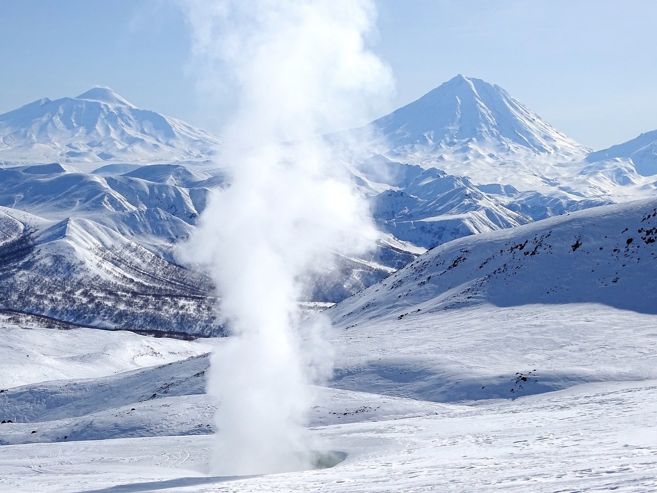 A fumarole rising in a mountainous, snowy landscape
