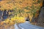 A mountain road with brilliant autumn leaves leading to a tunnel carved in the mountain