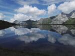 A still lake, with gray mountains, clouds and blue sky perfectly reflected in teh lake.