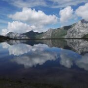 A still lake, with gray mountains, clouds and blue sky perfectly reflected in teh lake.