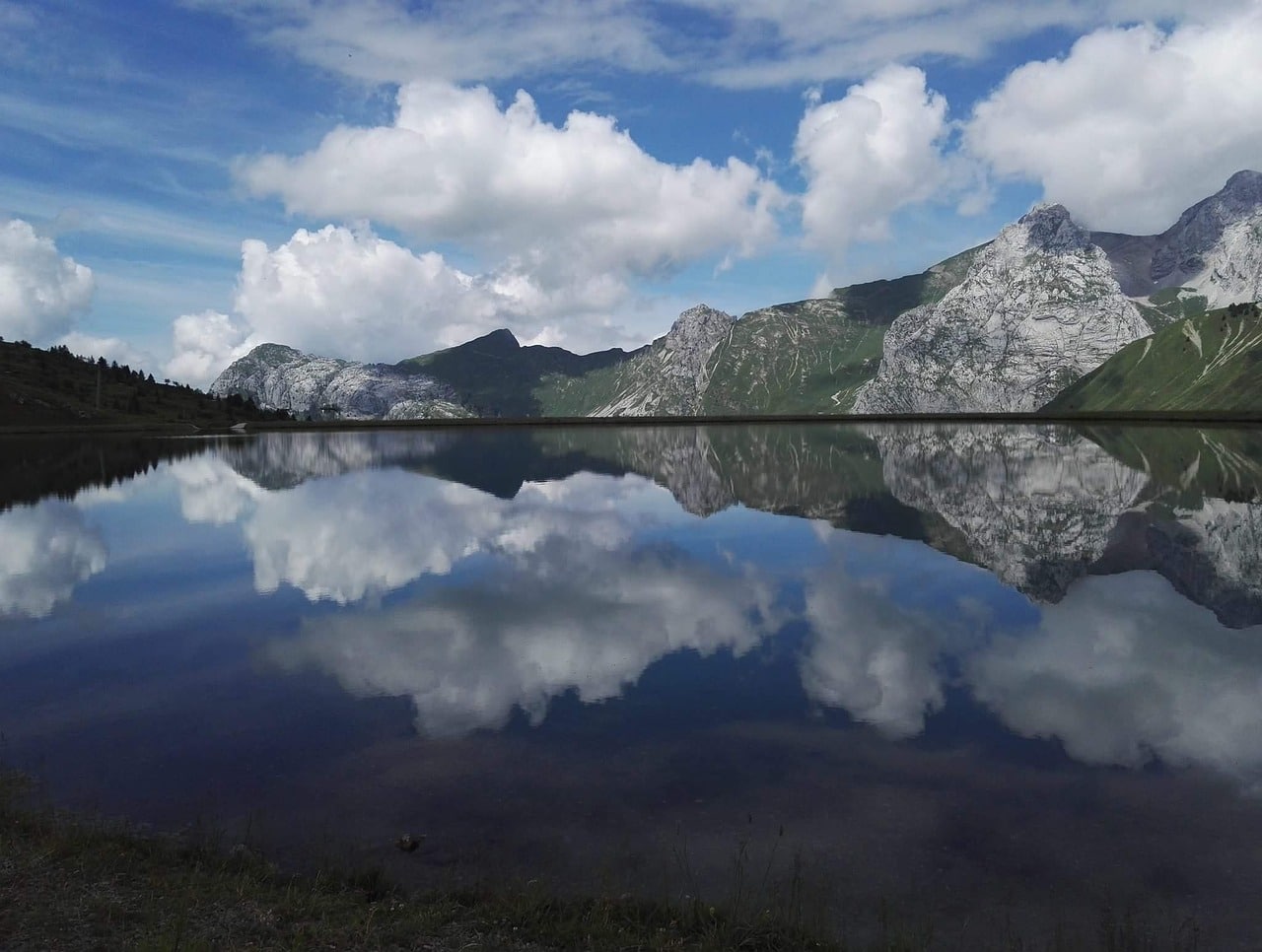A still lake, with gray mountains, clouds and blue sky perfectly reflected in teh lake.