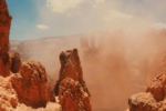 Close-up of a red rock canyon with high spires and blue sky in a dust storm.