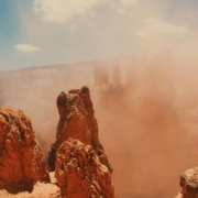 Close-up of a red rock canyon with high spires and blue sky in a dust storm.